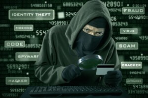 Stock photo of criminal holding magnifying glass and credit card with words in the background such as identity theft, code, spyware, hacker, fraud, virus, scam, cracker